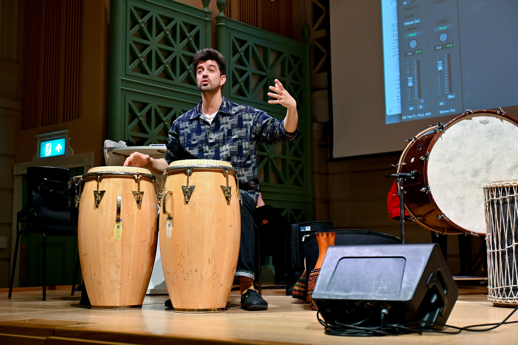 A man playing on drums and teaching to an audience on stage.